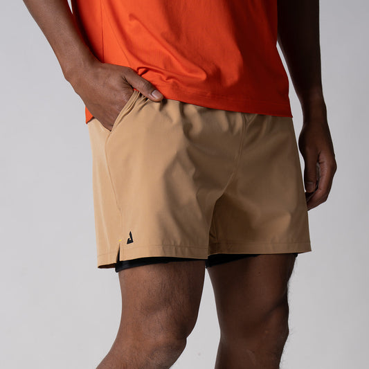 Gray background, close up image of a male model wearing a pair of JOOLA men's 2 in 1 shorts, latte color.