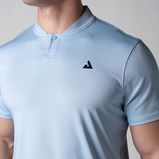 Gray background, close up image of the black JOOLA trinity logo about the left chest of a male model wearing the JOOLA Men's Court Polo, Blue Breeze.