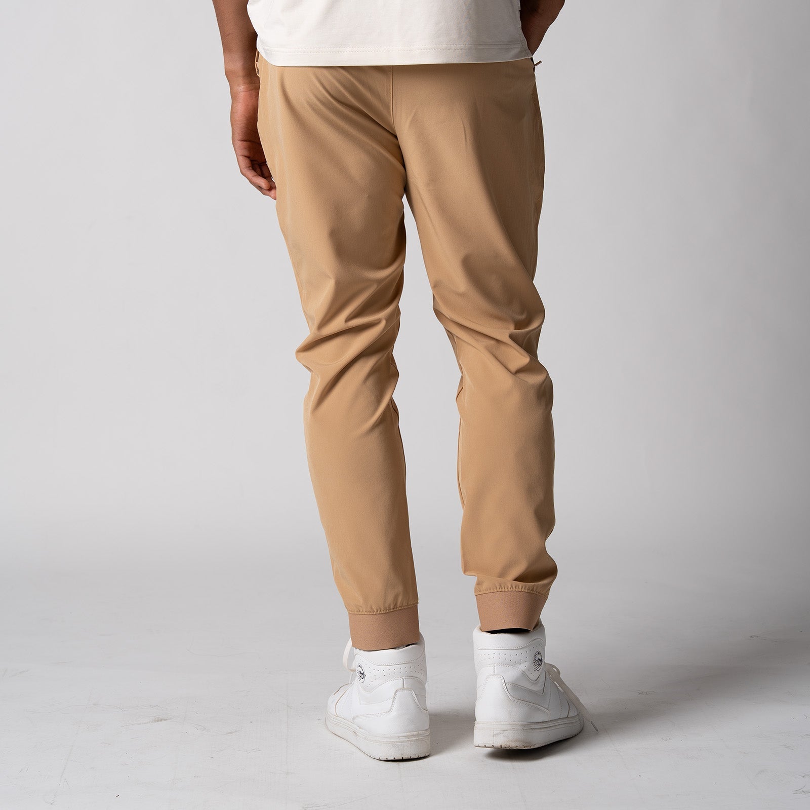 Gray background, male model wearing a pair of JOOLA men's club joggers, latte color.