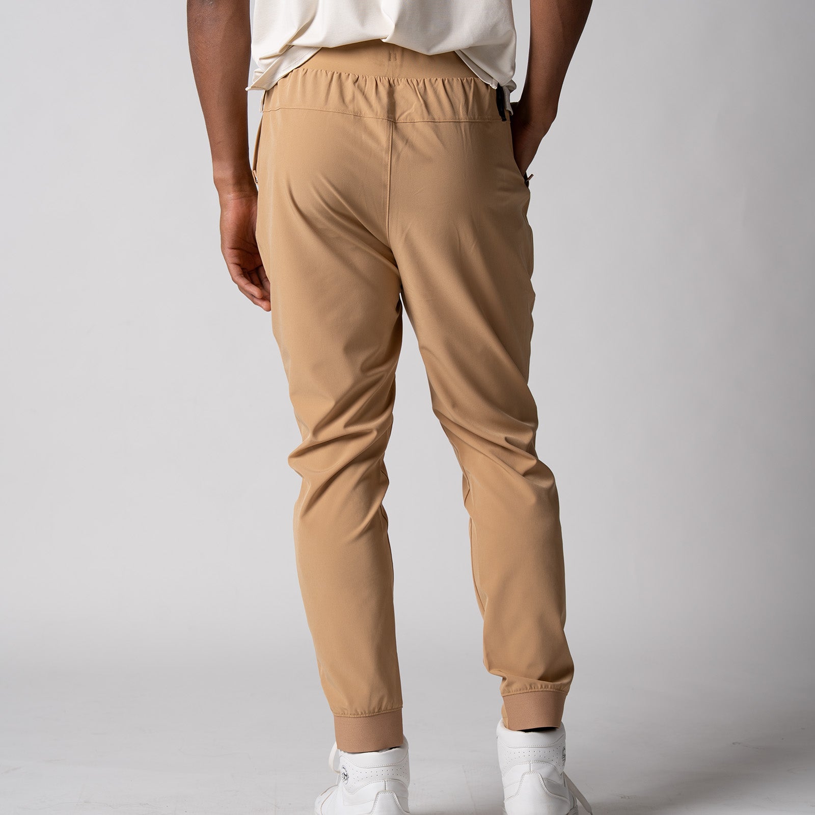 Gray background, image of a male model showing the back of a pair of JOOLA Men's Club Joggers, latte color.