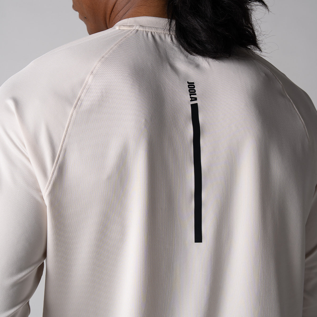 Gray background, close up image of the vertical JOOLA logo running down the back of a JOOLA Men's Court Long Sleeve shirt, sandstone.