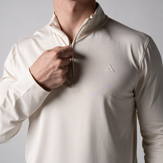 Gray background, close up image of a male mode holding the zipper of a JOOLA men's quarter zip pullover, sandstone color.