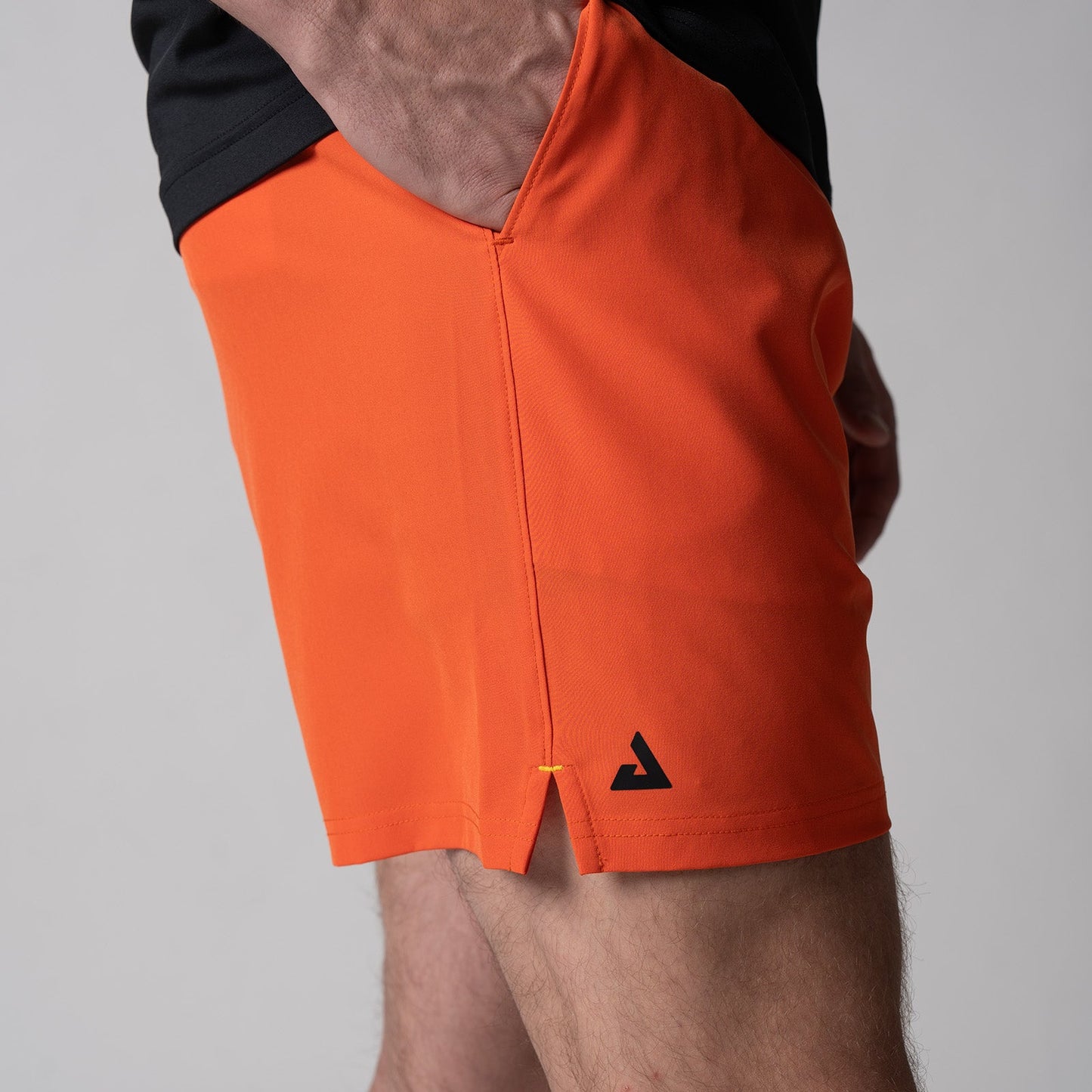 Gray background, close up of a black JOOLA trinity logo on the right leg of a pair of Men's Woven Short, poppy red.
