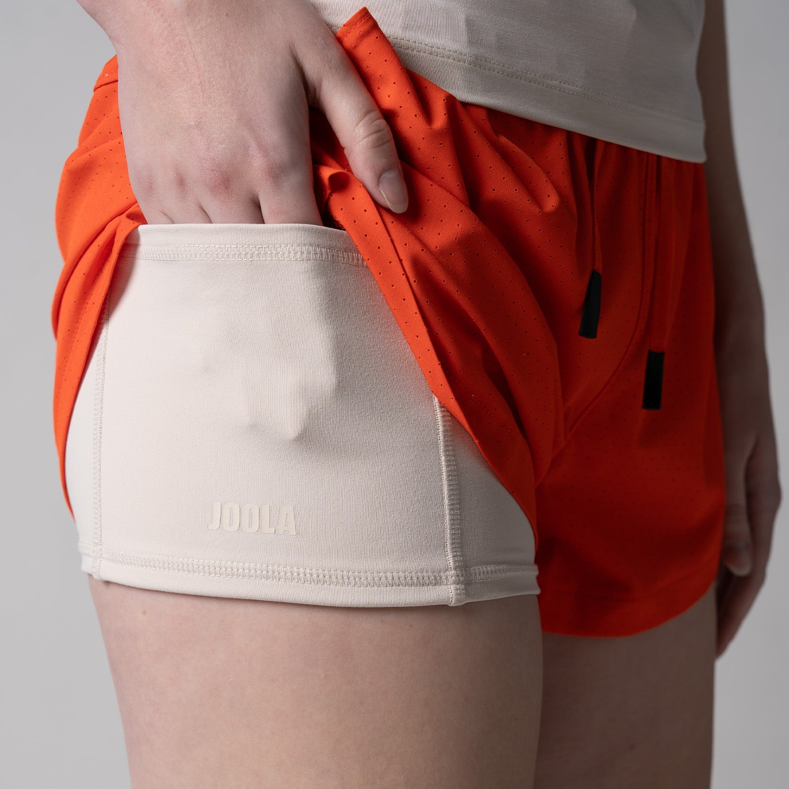 Close up of the hidden under shorty pocket in a pair of JOOLA women's court 2 in 1 shorts, poppy red.