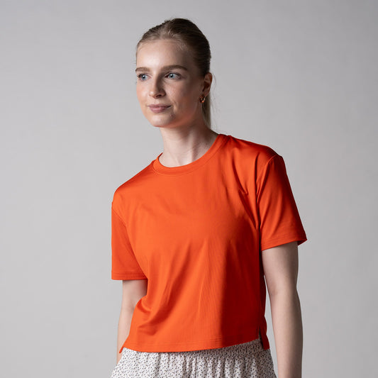 Gray background, female model wearing the JOOLA Women's Court Crop Tee, poppy red.