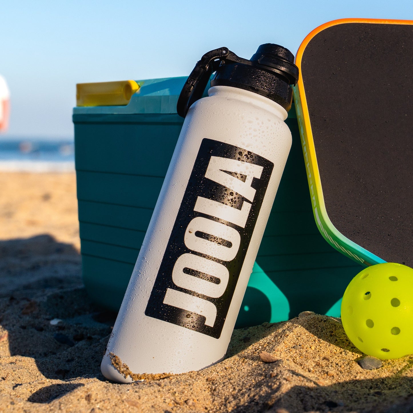 JOOLA Water bottle leaning up against a cooler on a beach.