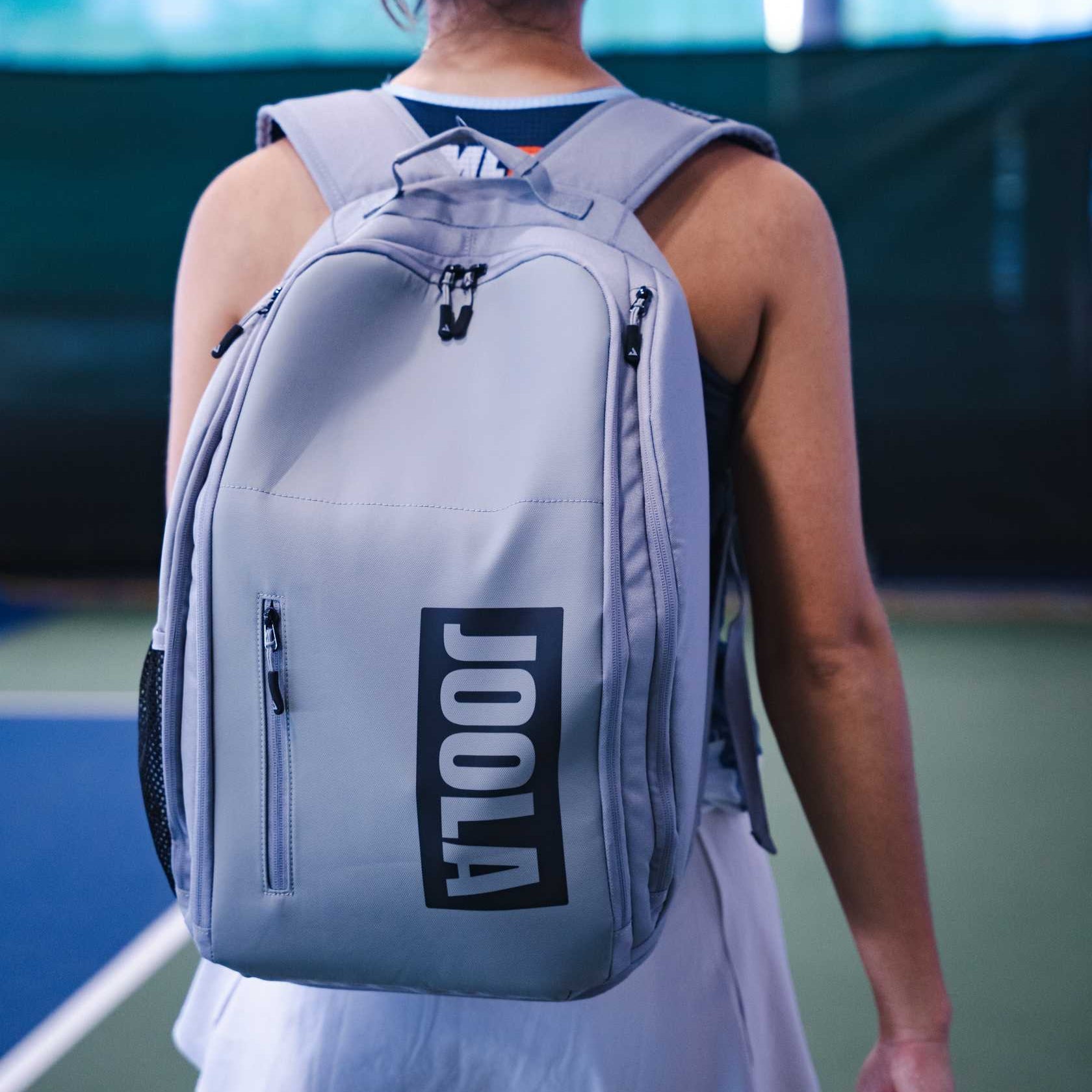 Person wearing a gray backpack with 'JOOLA' logo on a pickleball court.