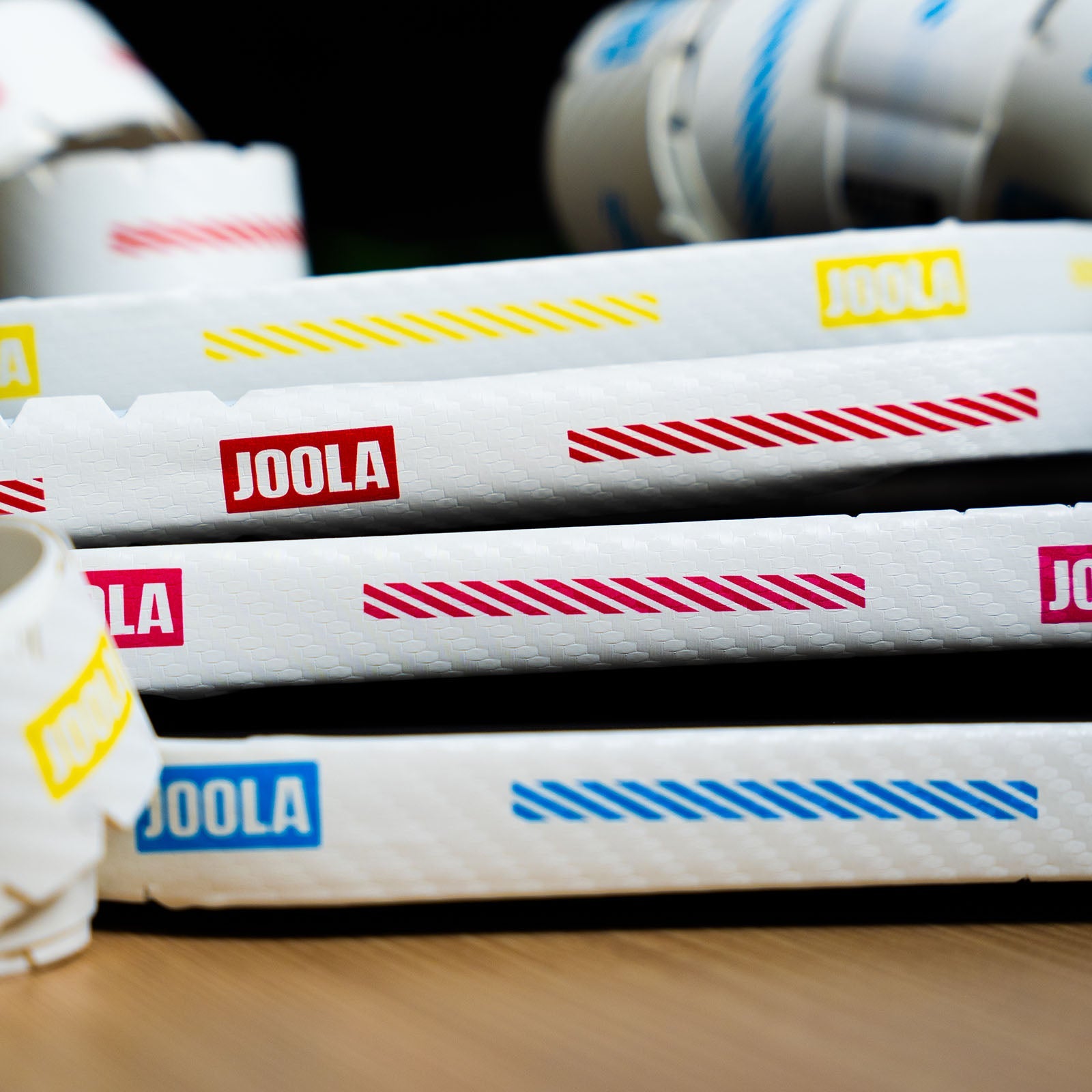 Stack of JOOLA Pro IV pickleball paddles with colorful stripes on a blurred background.